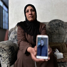 A woman holds out a phone with a picture of her son
